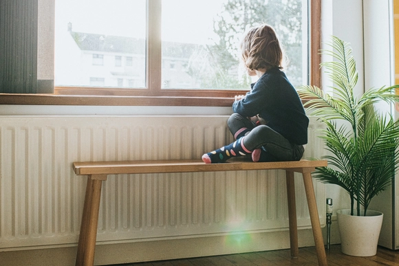 Kind sitzt auf Bank und schaut aus Fenster